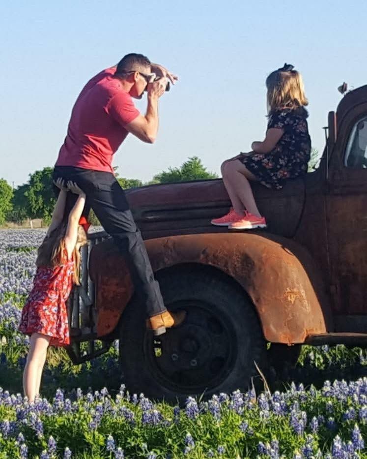 Danny photographing Laura on an old rusted truck in a field of bluebonnets